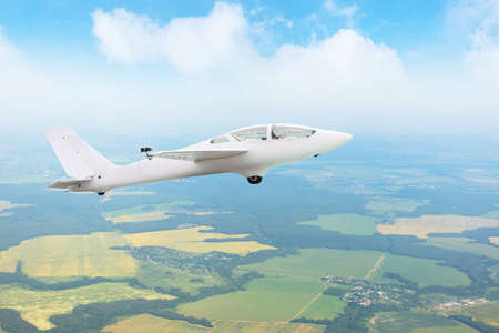 Glider flying high in the sky over fields and forests, aerial view