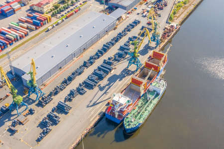Aerial top view huge cargo ship moored at the pier at the port, loading goods, metal in aluminum rolls, concrete and other solid raw materials.の写真素材