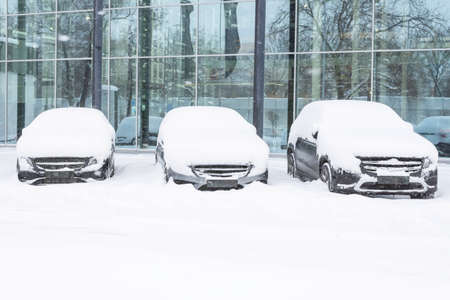 Snow covered of cars in the parking lot. Urban scene, snowstorm. Clean automobile from the snowの写真素材