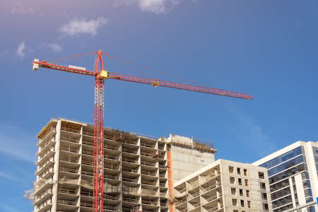 View of a building with high construction cranes and nearby a glass tower, built houses