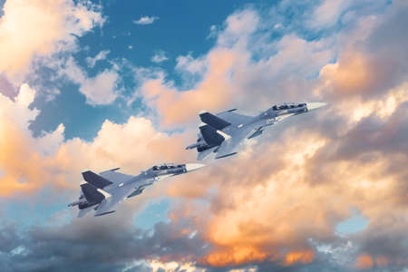 A pair of tandem military fighter jets fly in the sky against the backdrop of beautiful clouds at sunsetの写真素材