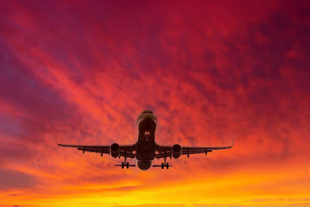 Airplane flying against the background of a bright red orange texture sky at dawn in the morning