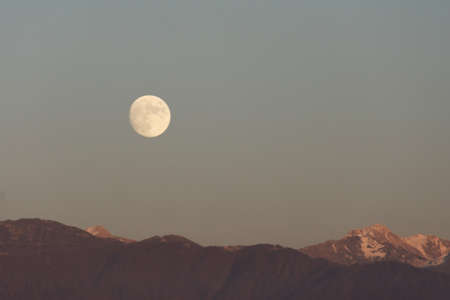 Full moon rises over mountain range evening skyの写真素材