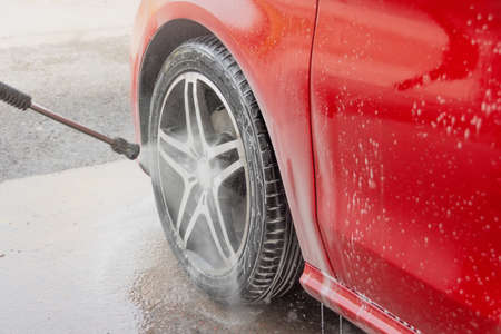Washing red car in a self-service car wash station. Wheel and tire rubber closeup. Car wash...