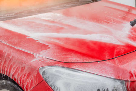 Washing a red car with foam and water jet hood and frontの写真素材