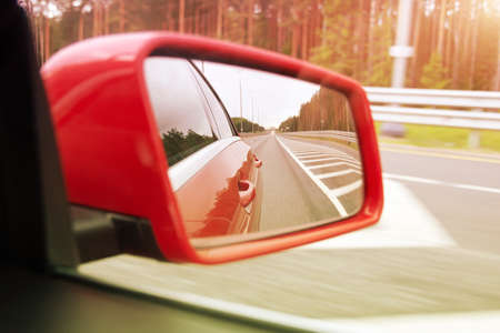 Side rearview mirror of a red car, roadside and highway reflection