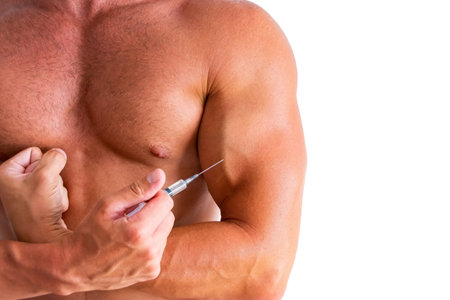 Bodybuilder holding an injection of a steroid syringe to his chest. Strong athletic rough muscular man pumps up abdominal muscles, exercising, doing fitness and bodybuilding, healthyの写真素材