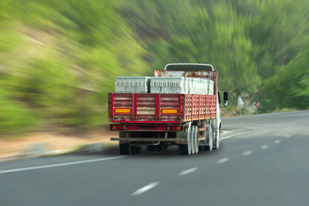 Truck with a trailer and foam blocks loaded into it, a building material, drives along a highway in the middle of a forest with the effect of speed motion blurの写真素材