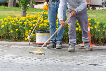 The construction technician is working by leveling the concrete floor to be smooth, leveling concrete in the cracks of paving stones on the highwayの写真素材