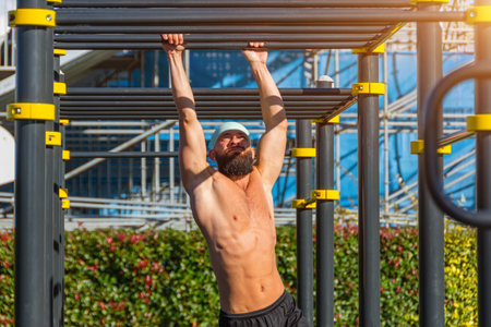Muscular man in a bandana hanging on the stairs intercepted on the rungs with his hands in the park...