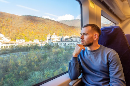 Young man holds his hand to his chin and looks enjoying the views of nature and small town in the valley riverの写真素材