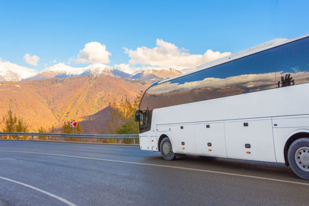 White tourist bus rides at a turn along a serpentine road against the backdrop of snow-capped mountain peaksの写真素材