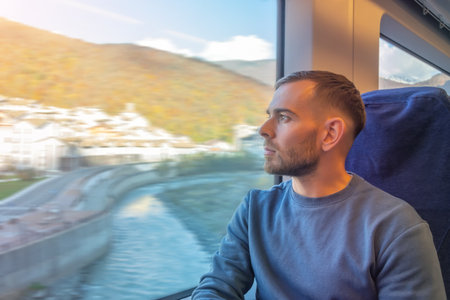 Young man looks enjoying the views of nature and small town in the valley river. Ride on a commuter trainの写真素材