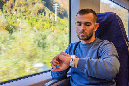 Middle-aged man looks at his watch to find out what time it is on the way, outside the window is a...