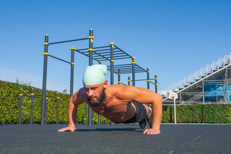 Muscular man doing calisthenic exercise push-ups from the floor on the sports ground in the city parkの写真素材