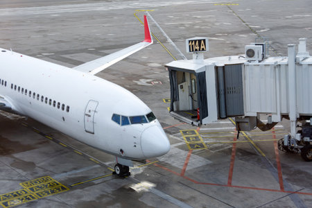 The aircraft is parked and the jet bridge is approaching the aircraft to unload passengers at the arrival terminalの写真素材