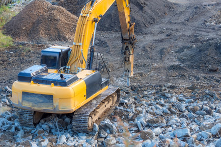 Yellow excavator with a jackhammer on the boom destroys the remains of a building on a pile of...