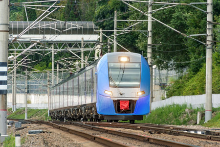 Suburban electric train of blue color goes from a distance with the headlights on along the way...