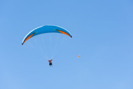 Two paraglider tandem fly against the blue sky, tandem paragliding on distance guided by a pilot