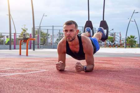 Man on the sports ground stands in a plank position, an exercise on the press, leaning on the elbows...
