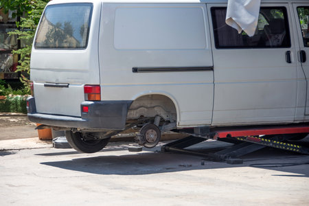Minibus with rear wheel removed, lifted by hydraulic jack, car repair next to service garage. Rear back viewの写真素材