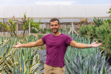 A young male gardener smiling with his arms outstretched shows his plants and possessions in a plant nursery. Sale of ornamental plants in the garden center, plantingsの写真素材