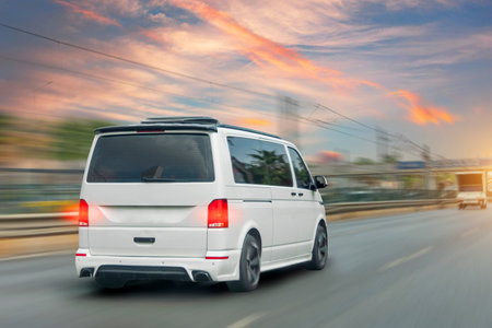 White modern passenger charter van with a small delivery moves fast on the highway to the urban suburbs. Business distribution and logistics express service. Mini bus rides along the highwayの写真素材