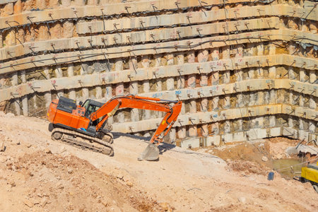Pit of a metro station with piles in the ground, working orange excavator dig and extract soilの写真素材