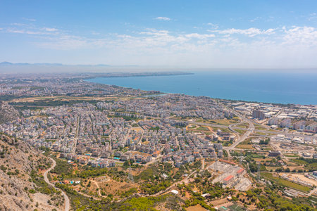 Flight over ridge mountain pass rocky terrain with bushes, bird's eye view overlooking the city, houses and buildings, roads and ships, Mediterranean coast, resort area, vacation tripの写真素材