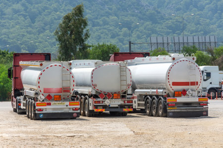 Parking row jam of trucks with fuel tanks in front of a warehouse and storage of huge tanks of raw material containers, next to the main highway.の写真素材