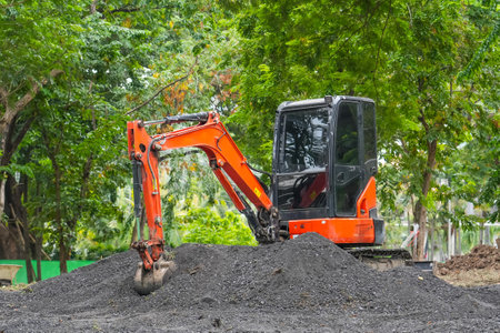 Orange mini excavator in operation digs and loads fertile soil in the park