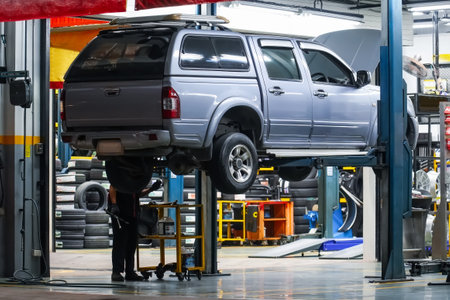 Pickup truck lifted into the air using a mechanical bridge jack in a service garage for car repair and maintenance at night time, back view.の写真素材