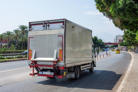 Small truck with a folding lift loader for goods rides along the road in the city delivering goods and foodの写真素材