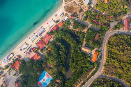 Tropical island with a sandy azure bay and pier and a beach village settlement surrounded with roads by exotic green forests trees hills, aerial view.の写真素材