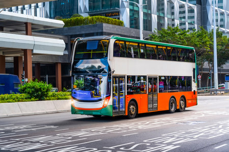 Double-decker city shuttle bus drives down the street among buildings.