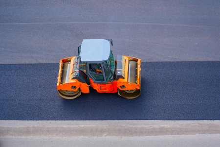 Road repair road roller machine rolls asphalt city street, aerial view.