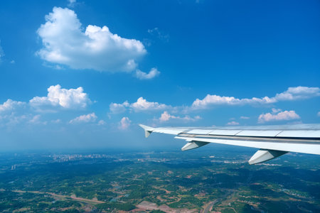 Wing of an airplane flying climb take off above flat cumulus clouds over terrain.の写真素材