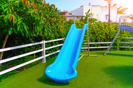 Blue children's slide in playground skate city park surrounded by green foliage.の写真素材