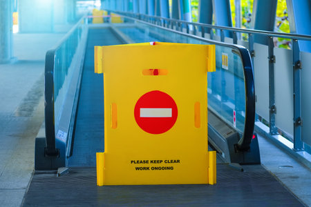 Yellow fence with a brick sign, passage is prohibited on a travellator, an elevated pedestrian crossing at the airport, railway stationの写真素材
