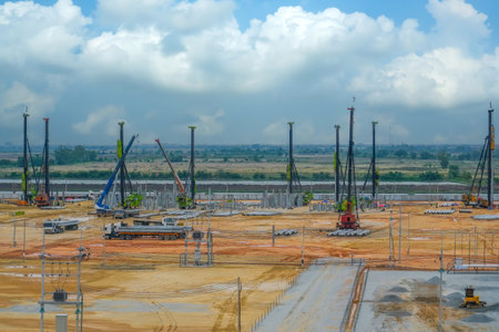 A busy construction site showcases several cranes and machinery working together on a project. The sky is partly cloudy, and machinery is located across the expansive area.の写真素材