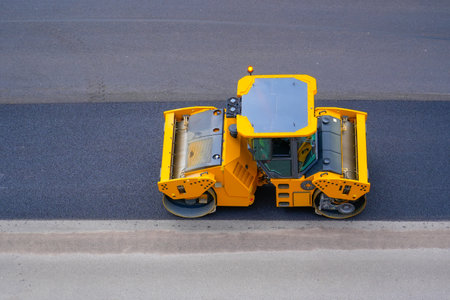 Road repair road roller yellow machine rolls asphalt city street, aerial view.の写真素材