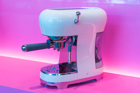 Contemporary coffee machine stands out with its sleek lines and shiny finish, showcased against a bright pink background. Ideal for coffee enthusiasts looking for a chic appliance.の写真素材