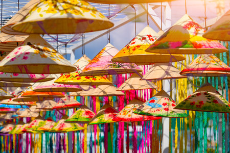 Numerous beautifully decorated Vietnam tradition hats hang above, creating colorful canopy at lively festival. The vivid colors and artistic designs attract visitors in a festive market environment.の写真素材