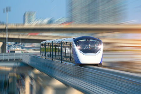 A sleek transit train glides along elevated tracks in a vibrant city, showing advanced design and technology during daylight hours, surrounded by skyscrapers.の写真素材