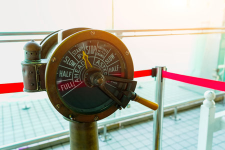 Antique brass ship telegraph is set to stop. The communication device is cordoned off from public access by a velvet rope and metal stanchion inside a modern building.の写真素材
