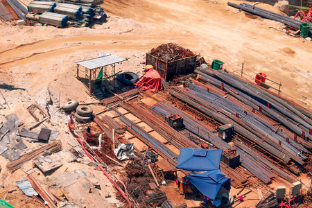 From an aerial perspective, a dusty construction site is shown. Workers are resting near piles of...