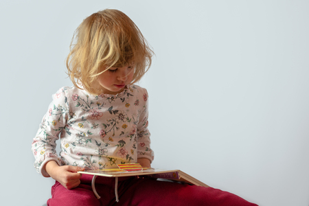 preschool girl reading book studio portrait on clean backgroundの写真素材