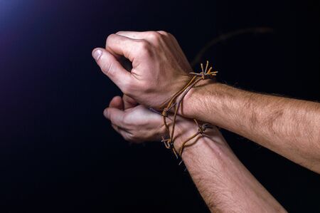 hands on a dark background wrapped in rusty barbed wireの写真素材