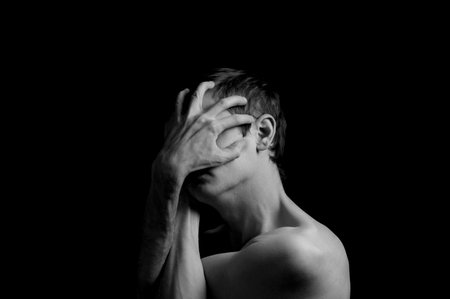 young man on a black background in a dramatic expressive poseの写真素材