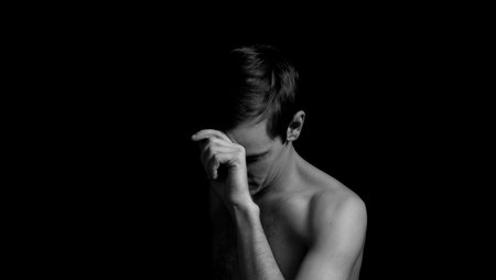 young man on a black background in a dramatic expressive poseの写真素材